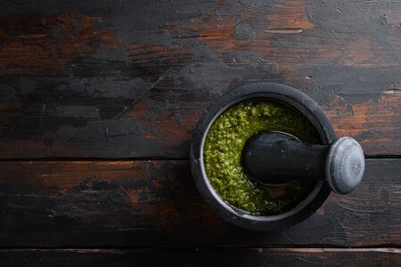 fresh Green basil pesto preparation in black mortar over old wood table copy space for text overhead.の写真素材