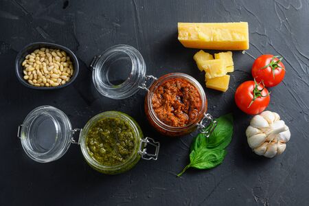 red and green Pesto alla Genovese , Basil Sauce resh home made and cooking italian recipe ingredients Parmesan cheese, basil leaves, pine nuts, olive oil, garlic, salt, tomatoes top view on black stone concrete surfaceの写真素材