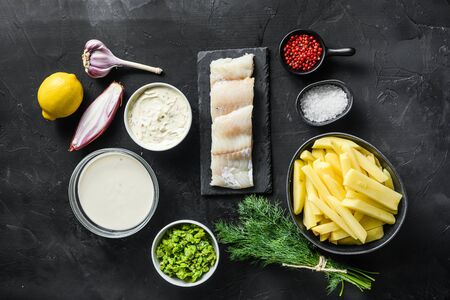 Organic fish and chips ingredients raw cod fillets on stone slate batter, potatoe, tartar sauce, minty mushy peas, lemon , shallot, mint, garlic, salt, peppercorns on black stone background overhead photo.の写真素材