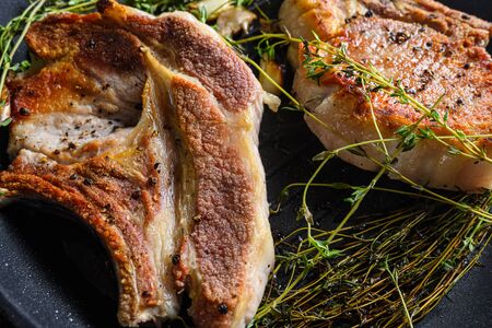 Grilled organic pork steak with herbs on bone in grill frying pan hot with smoke and hot oil just from fire, top view cooking bone with seasonings rustic metal background close upの写真素材