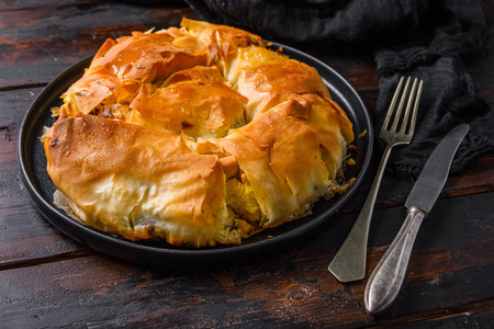 Homemade Greek spanakopita in on black plate filo spinach eggs feta side view on dark wooden...
