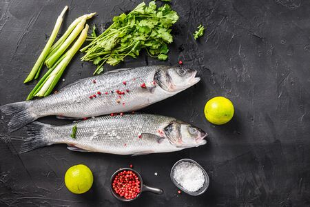 Set of whole raw seabass with spices and herbs ingredients on chopping board over black stone table top view space for textの写真素材
