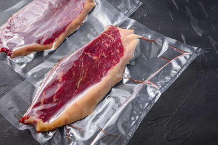 Picanha beef steak in vacuum sealed bag on black textured background, side view space for priceの写真素材