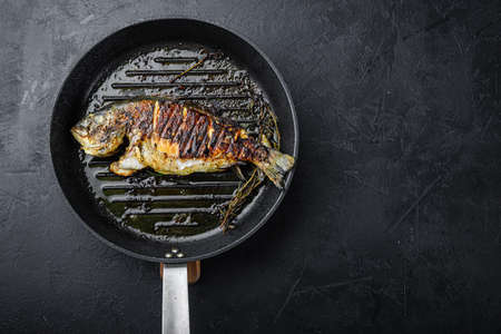 Grilled sea bream or dorado raw fish on grill hot pan over textured black background, top view with space for textの写真素材