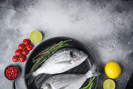 Raw sea bream or dorado raw fish on grill pan with ingredients on grey white textured background,...