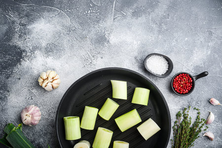 Raw braised Leeks on grill pan uncooked with herbs ingredients , on textured grey background top...
