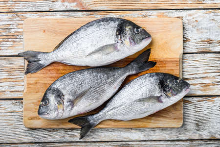 Raw dorada or sea bream on choppong board over white wood table top view.の写真素材