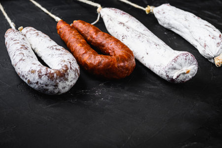 Traditional spanish sausages longaniza and chorizo on black background with space for text.