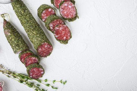 Traditianal fuet sausage in herbs with ingredients on white textured background with space for text.