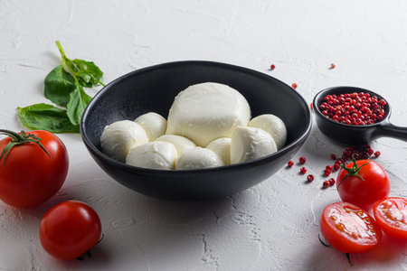 Mozzarella cheese in black bowl, basil tomato cherry balsamic black slate stone copy space. Ingredients for Caprese salad on white background close up selective focus.の写真素材