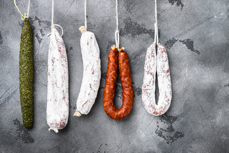 Spanish dry salami from a rack at market on grey textured background