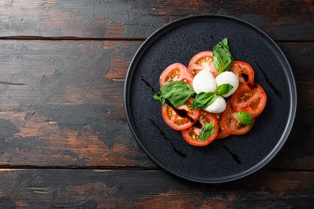 caprese salad with sliced tomatoes, mozzarella cheese, basil, olive oil. Served on black plate wood kitchen old rustic table top view flatlay space for textの写真素材