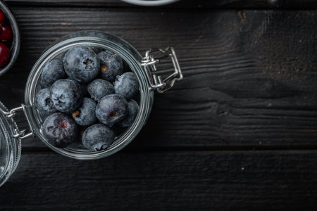 Ripe blueberry in glass jar, flat lay with space for text, on black wooden background.の写真素材