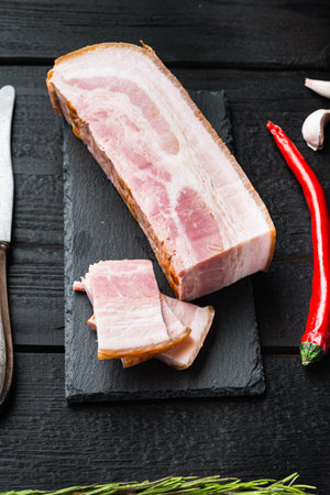 Bacon pancetta cut and sliced with herbs on black wooden table.の写真素材