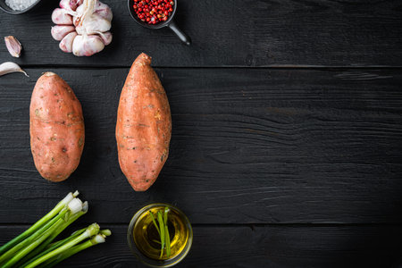 Raw whole sweet potatoe with ingredients, on black wooden background, flat lay with copyspace.の写真素材