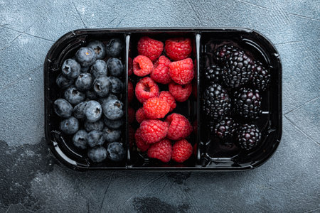 Ripe berries in tray from market, blueberries, raspberry with blackberry, top view, on gray backgroundの写真素材
