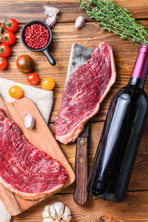 Picanha organic beef steaks over old american butcher cleaver with seasonings and red wine bottle on wooden table. Top view close up.の写真素材