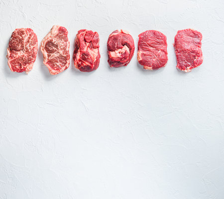 A set of different types of raw beef steaks: top blade, rump, chuck eye roll over white concrete background top view big size space for textの写真素材