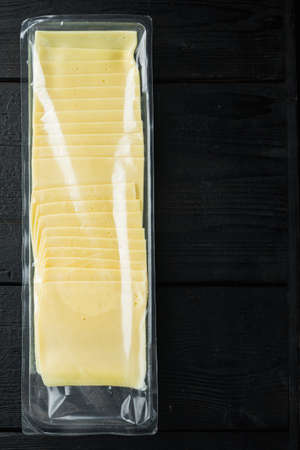 Slices of yellow cheese, sealed pack, on black wooden table with copy space for textの写真素材