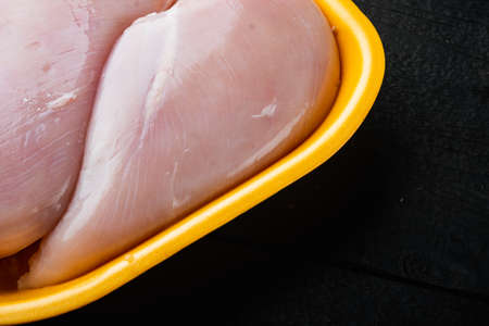 Fresh chicken breast meat in open tray, on black wooden table with copy space for textの写真素材