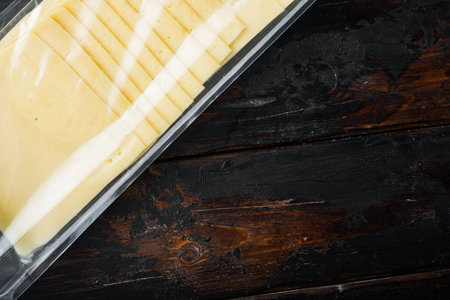 Slices of american cheese plastic pack, on dark wooden background with copy space for text