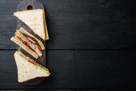 Sandwich with ham, cheese, tomatoe, lettuce, chicken meat and toasted bread, on black wooden table, top view with copy space for textの写真素材