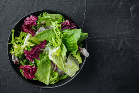 Bowls with mixed shredded salad lettuce fresh leaves, on black background, top view flat lay with...