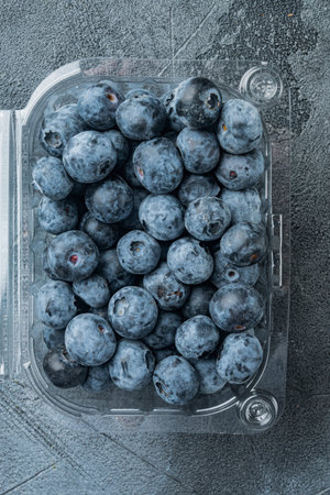 Freshly gathered blueberries, in tray, on gray background, top view flat lay