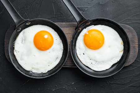 Fried eggs with cherry tomatoes and bread for breakfast in cast iron frying pan, on black background, top view flat layの写真素材