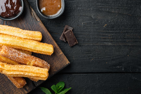 Traditional Spanish dessert churros with sugar and chocolate set, on black wooden table background, top view flat lay with space for text, copyspaceの写真素材