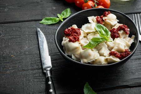 Appetizing ravioli with tomato sauce, cheese and basil set with basil parmesan and tomatoe in black bowl, on black wooden table background, with copyspace and space for textの写真素材