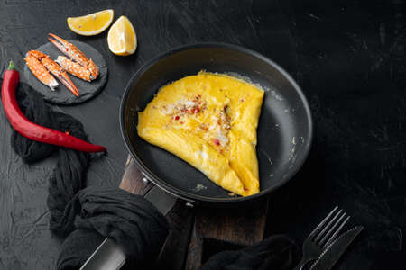 Thai Asian omelette, fresh red chilli, brown and white crabmeat, lemon, Cheddar cheese and eggs, on frying iron pan, on black backgroundの写真素材