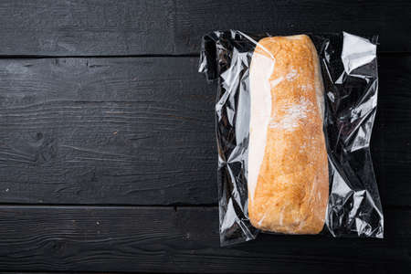 Ciabatta panini bread in a plastic bag, on black wooden table background, top view flat lay, with copyspace and space for textの写真素材