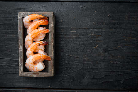 Whole fresh peeled cooked prawns, shrimps set, in wooden box, on black wooden table background, top view flat lay, with copyspace and space for textの写真素材
