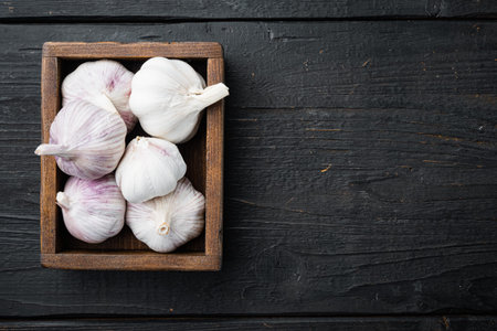 Pile of organic farm garlic set, in wooden box, on black wooden table background, top view flat lay,...