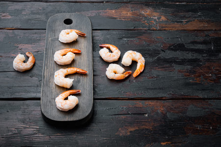 Boiled peeled king prawns set, on wooden cutting board, on old dark wooden table background, with...