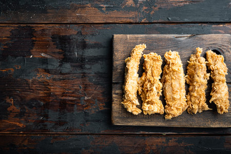 Crispy fried chicken broast cuts on old dark wooden table, top view, with copy space.