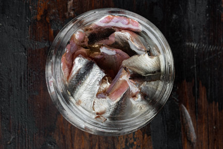 Pickled salted anchovies fillet set, in glass jar, on old dark wooden table background, top view flat layの写真素材