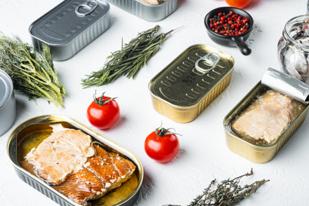 Salmon, tuna, trout mackerel and anchovy - Canned fish in tin cans set, on white background with herbs and ingredientsの写真素材