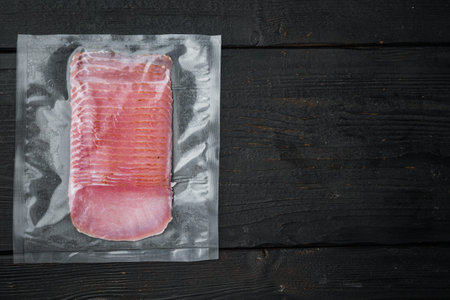 Dried pork meat slices set, vacuum packed, on black wooden table background, top view flat lay, with...