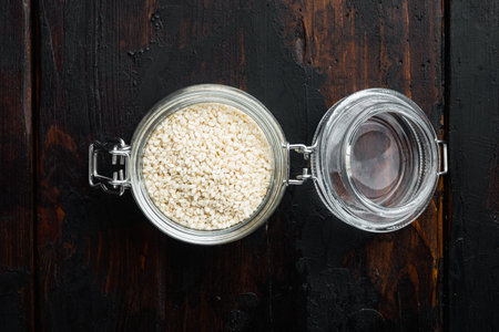Organic natural sesame seeds set, in glass jar, on old dark wooden table background, top view flat...