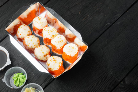 Tasty sushi rolls in disposable boxes set, on black wooden table background, with copyspace and...