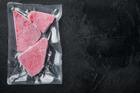 Frozen Tuna fish steak in a vacuum plastic package set, on black stone background, top view flat lay, with copyspace and space for textの写真素材