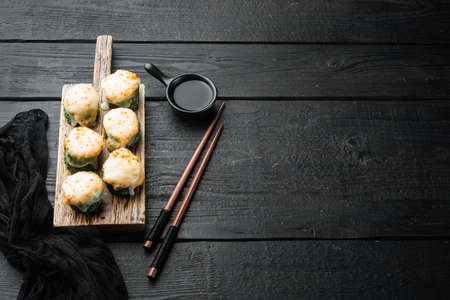 Baked sushi roll with shrimp and masago caviar cap. Traditional sushi restaurant dish set, on black wooden table background, with copyspace and space for textの写真素材