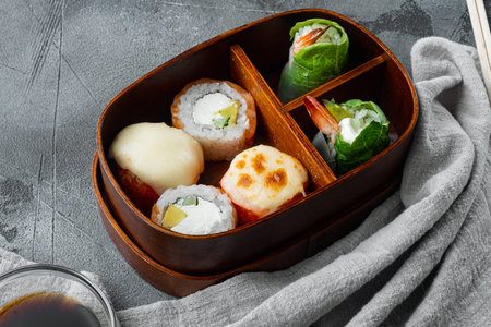 Japanese Meal in a Box Bento with sushi roll eice avocado salmon fish set, on gray stone background,...