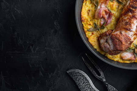 Baked pork fillet loin with potatoe and herbs set, on frying cast iron pan, with barbeque knife and meat fork, on black stone background, top view flat lay, with copyspace and space for textの写真素材