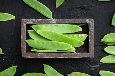 Fresh organic mangetout, also known as sugar snap pea set, in wooden box, on black stone background,...