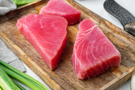 Fresh raw tuna fish steak with green pea, sesame and spring onions set, on wooden tray, on white stone backgroundの写真素材