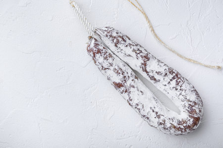 Salami sausage fuet on white textured background with copy space.
