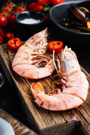 seafood king prawns on wooden board with spices over black wood table, food photo.の写真素材